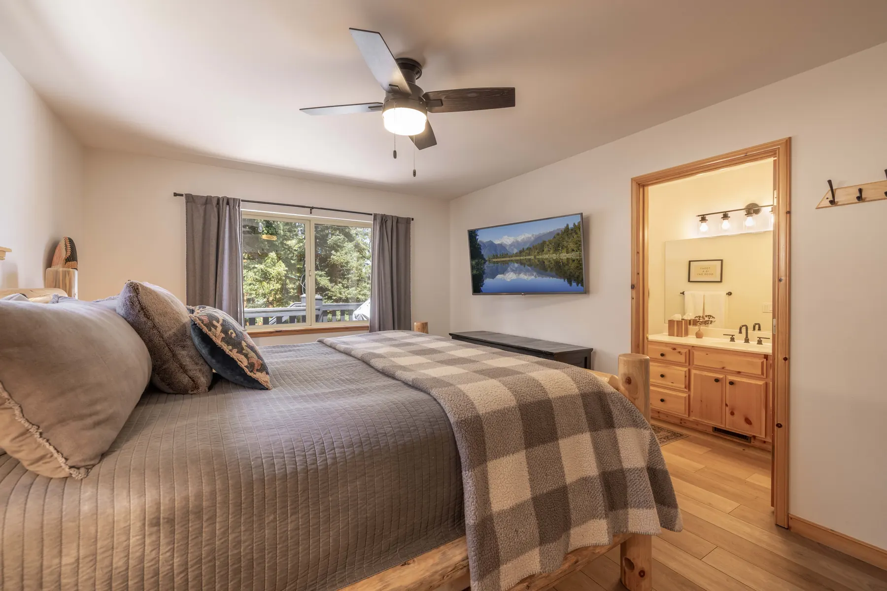 Primary bedroom at Pine Grove Cabin with a king bed, ceiling fan, mounted TV, and en-suite bathroom