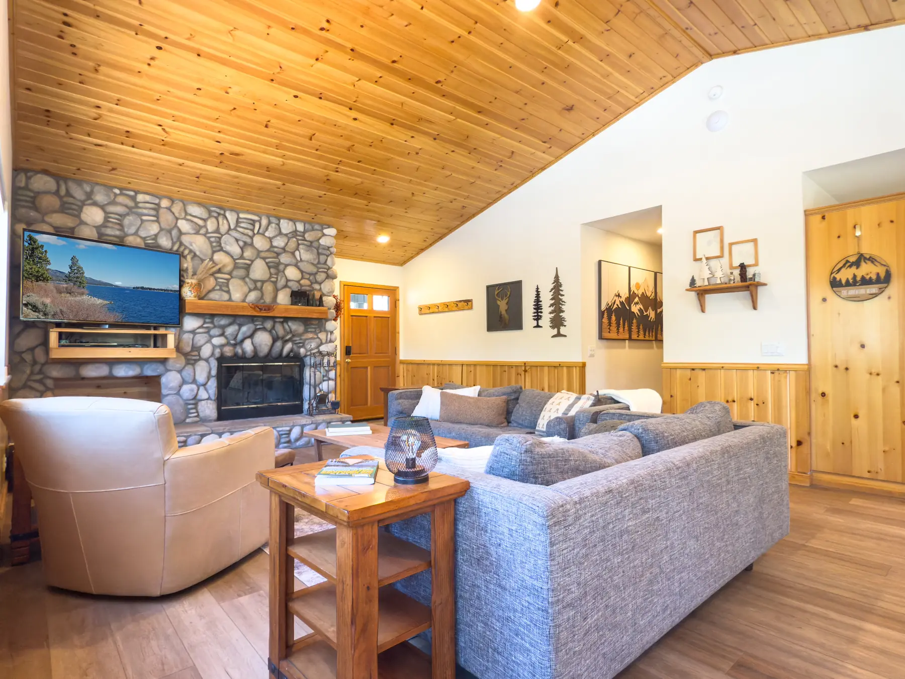 Living room at Pine Grove Cabin showing the stone fireplace, mounted TV, and mountain-themed wall art