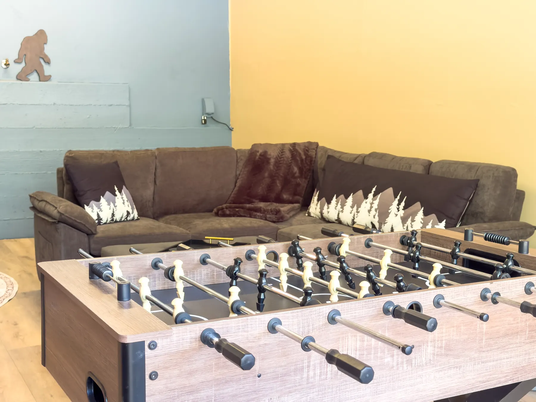 Close-up of the foosball table and sectional couch with mountain and Bigfoot pillows in the Sasquatch Den at Pine Grove Cabin