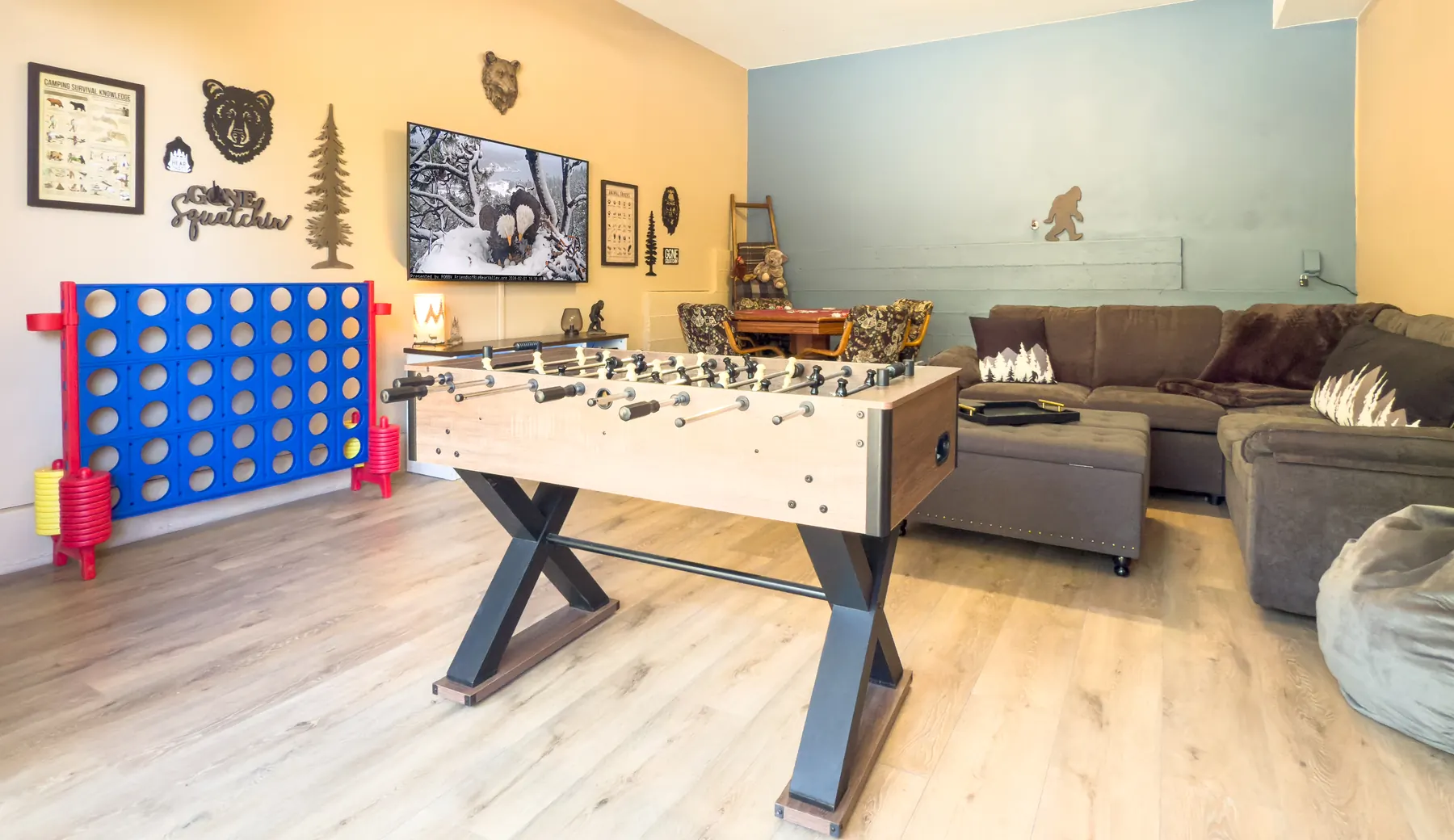 The Sasquatch Den at Pine Grove Cabin, a downstairs game room with a foosball table, jumbo Connect Four, sectional couch, and Bigfoot-themed wall decor